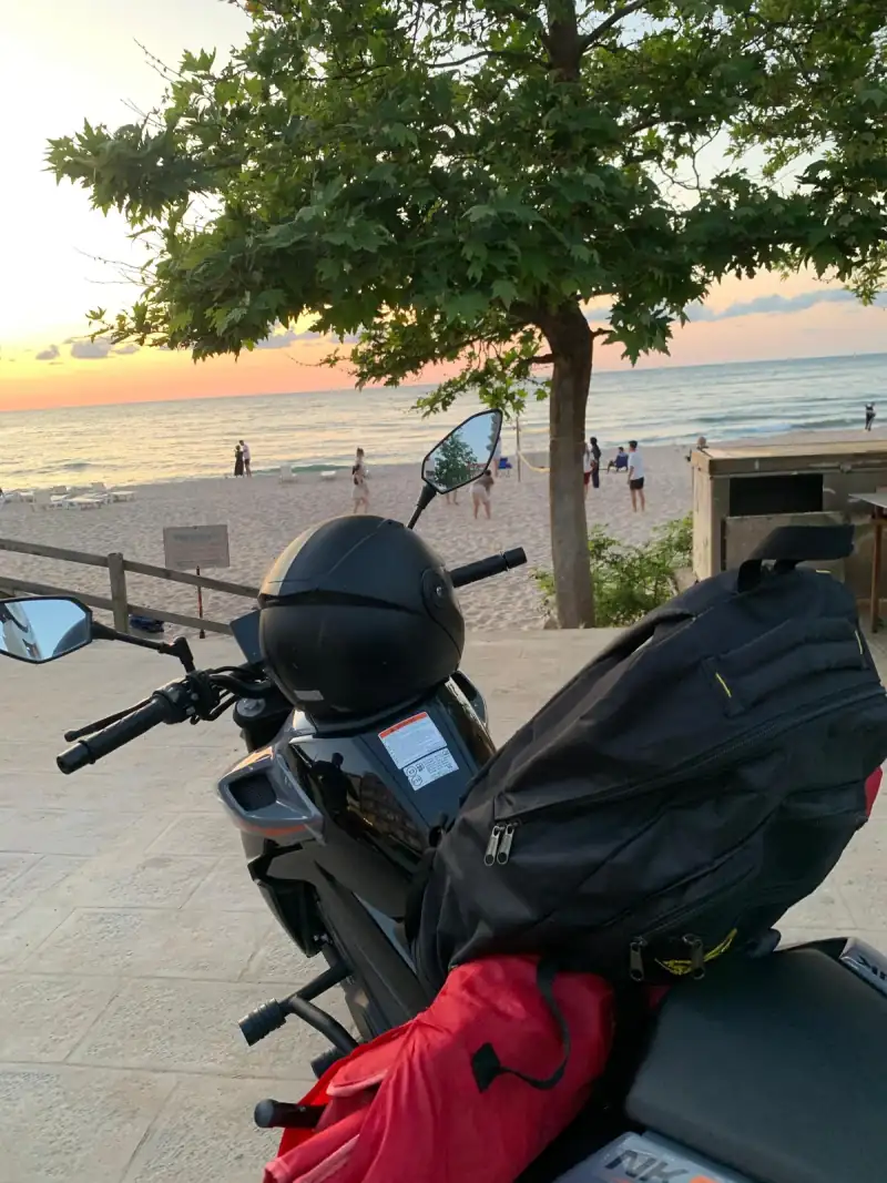 A CFMOTO 250NK with a helmet on the tank, parked above Çakraz beach at sunset