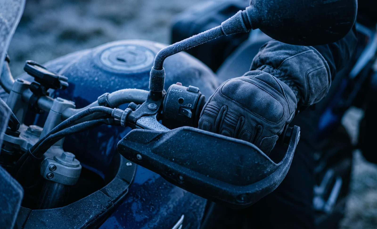 A gloved hand on a heated grip with a handguard fitted, frost visible on the mirror stalk on a cold morning