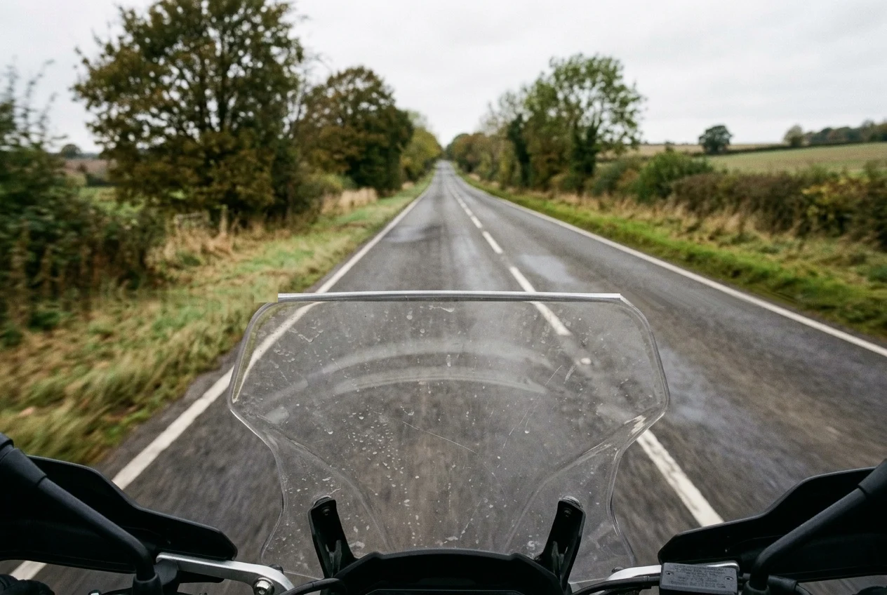 Rider's-eye view over the top edge of a clear motorcycle windscreen, with the road ahead seen above the edge rather than through the screen
