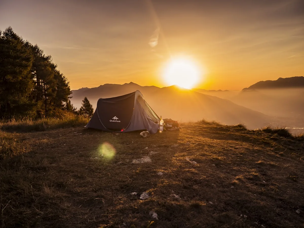 A solo camping tent illuminated from within under a starry night sky in a remote mountain valley