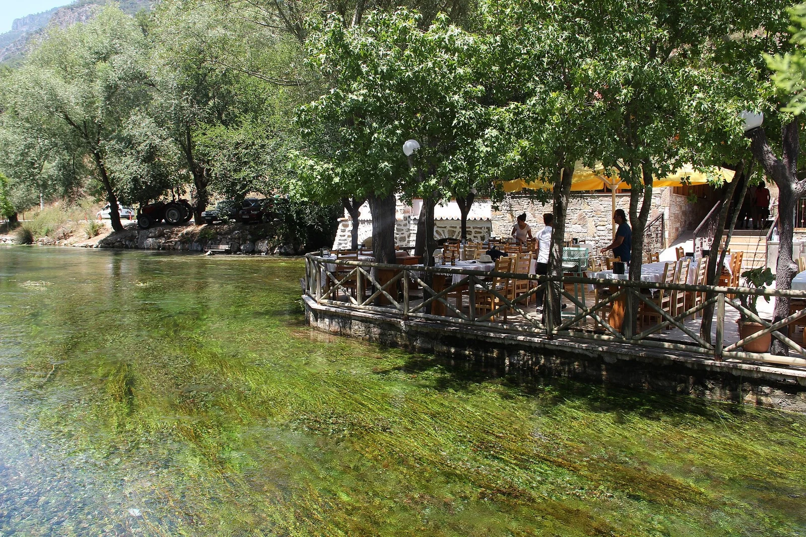 The clear Azmak river at Akyaka with restaurant terraces under the trees